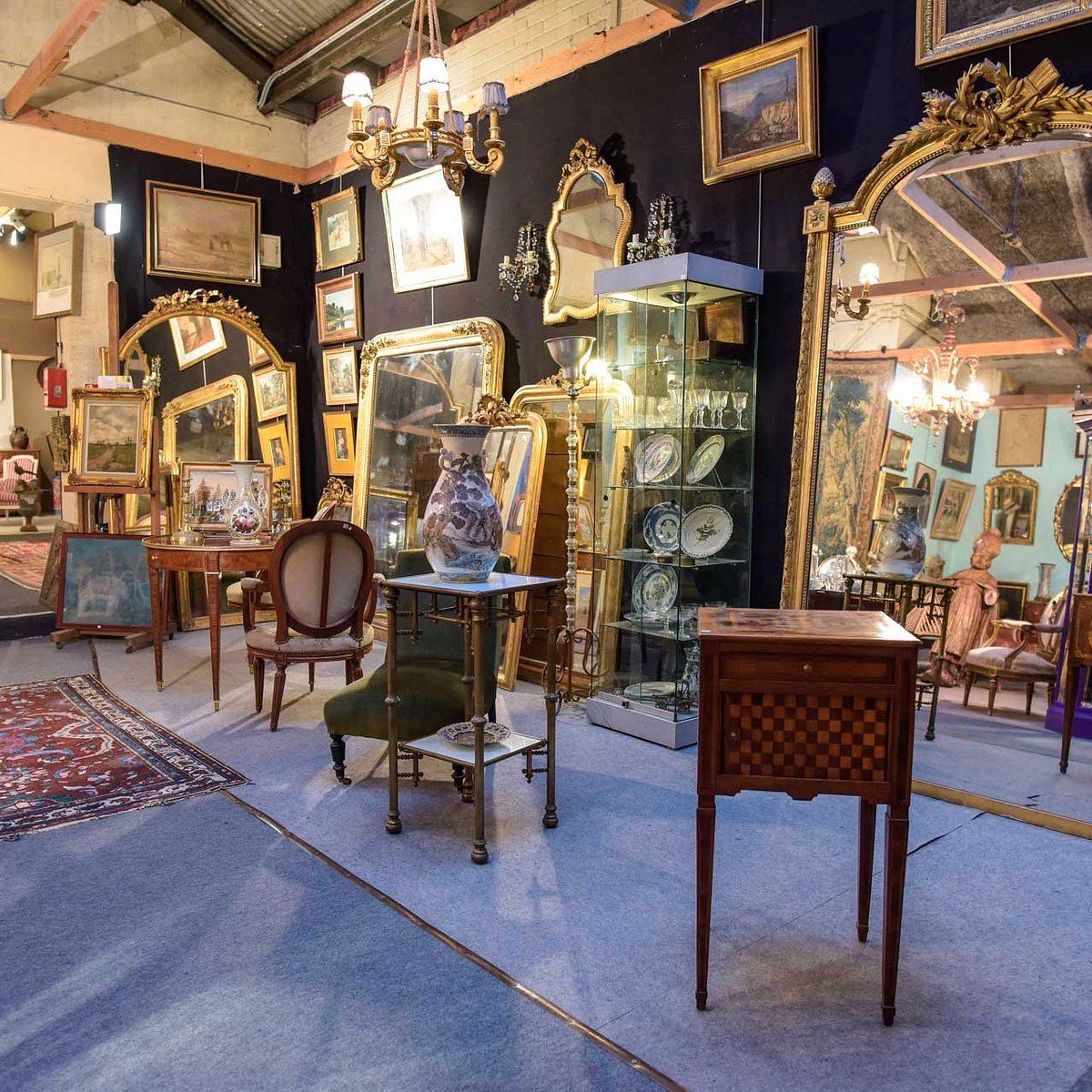 Galerie d'antiquités : miroirs dorés, vitrines, table en marqueterie et sièges anciens